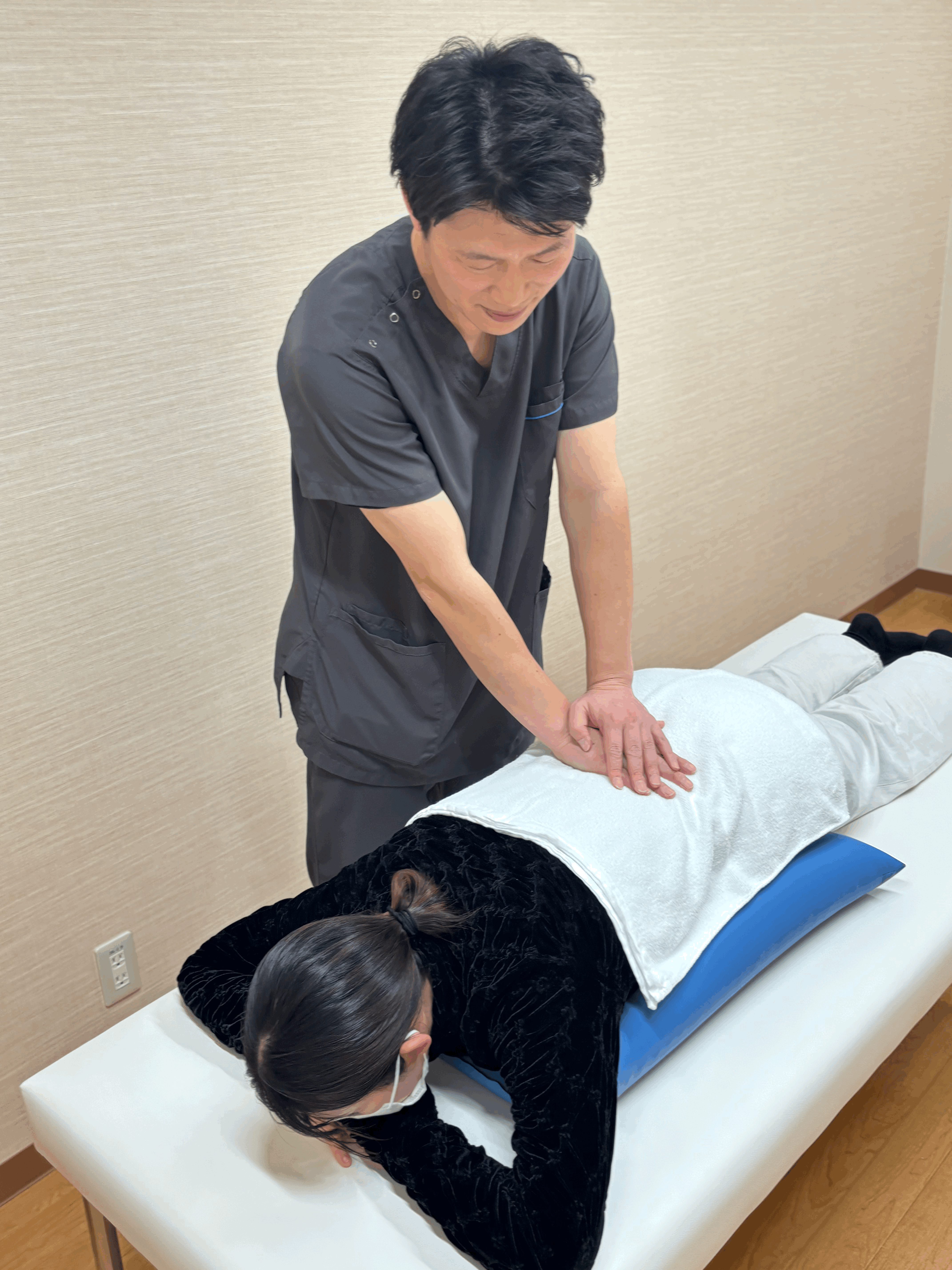 オーダーケアサロンVoiceの代表が、うつ伏せの腰痛の女性に対して、腰のあたりに手を当て、マッサージをしている写真。