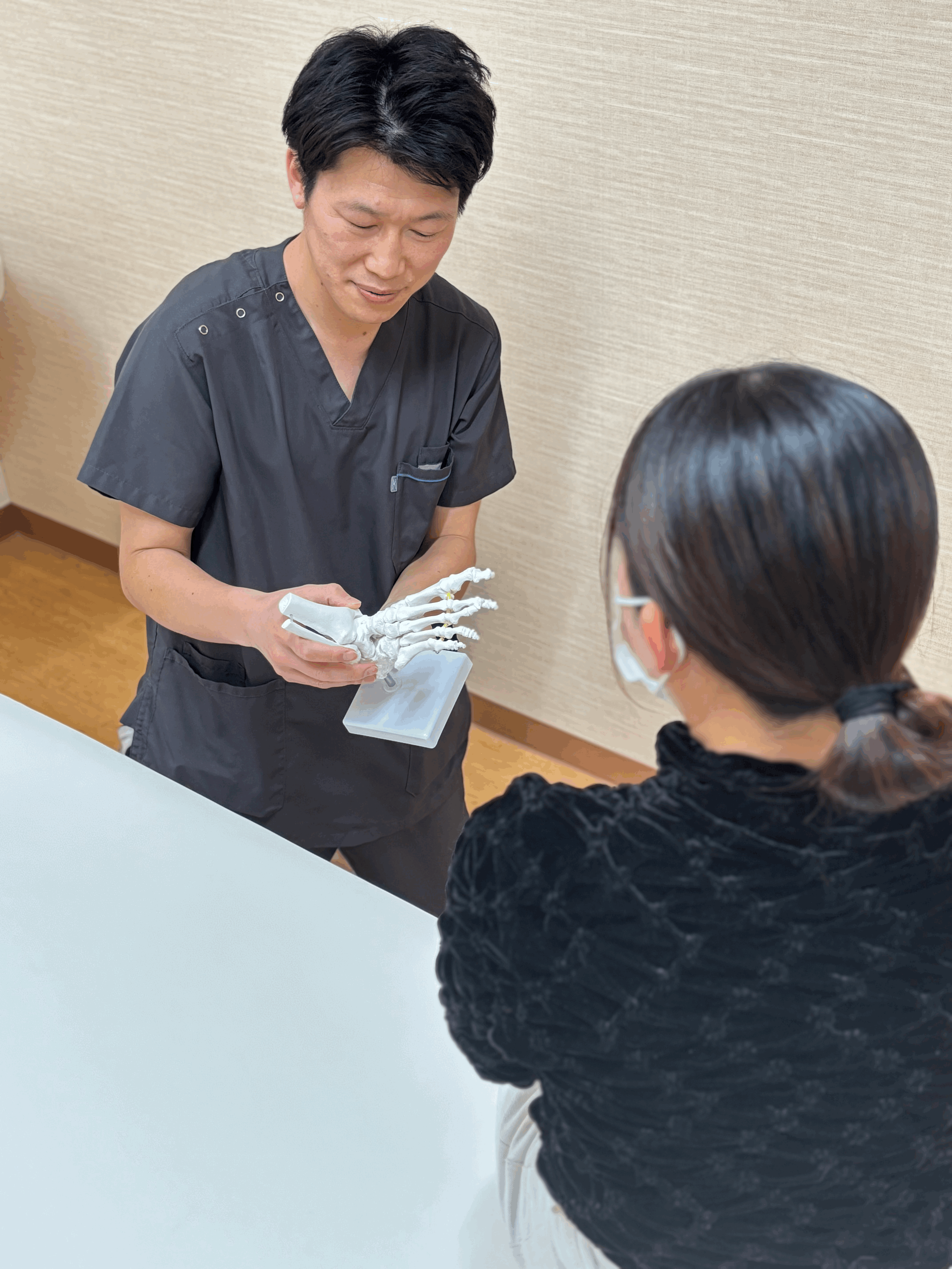 クライアントに対して、骨模型を見せながら、腰痛の原因について説明している。