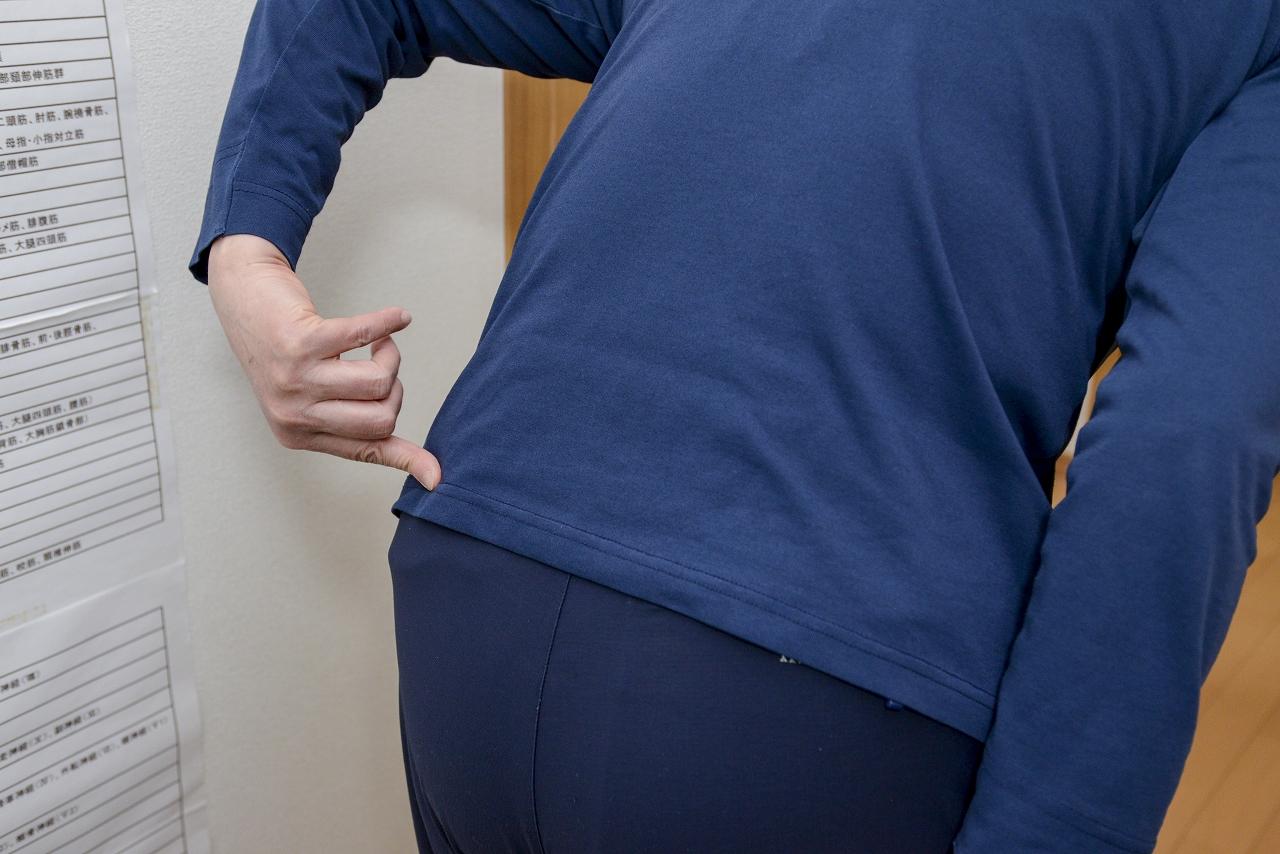 【腰痛の動作痛の検査】立位前屈して痛い個所を指さしている