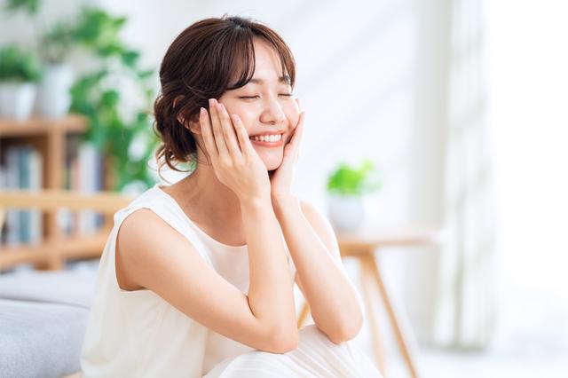 エイジングケアを受けて、潤った肌を両手で押さえてほほ笑む女性