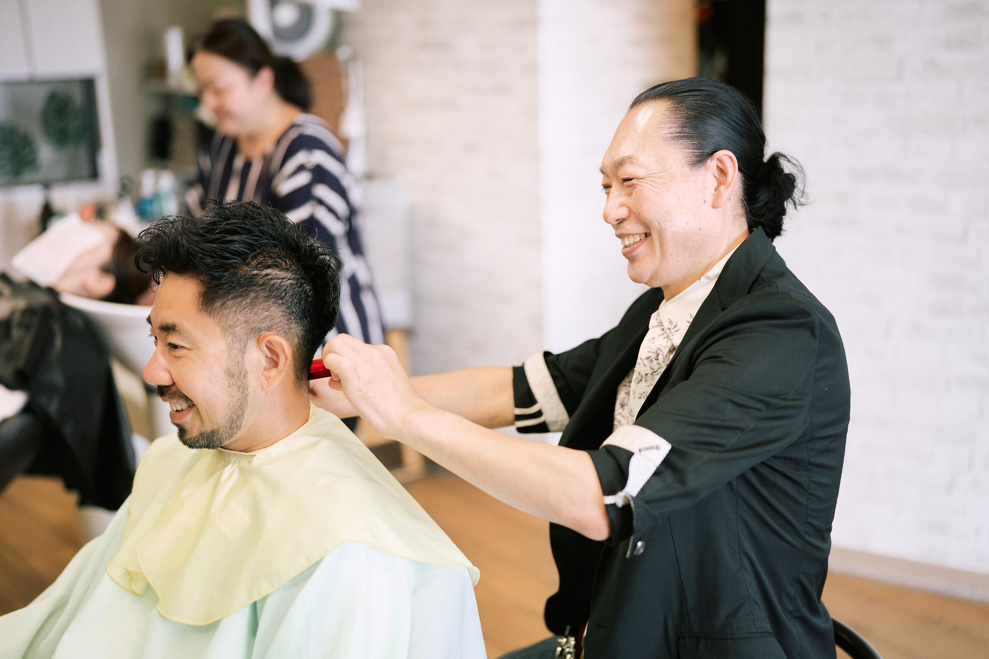 男性客と談笑しながら調髪をするアピスフォーヘアーオーナー / スタイリスト 成田 晃