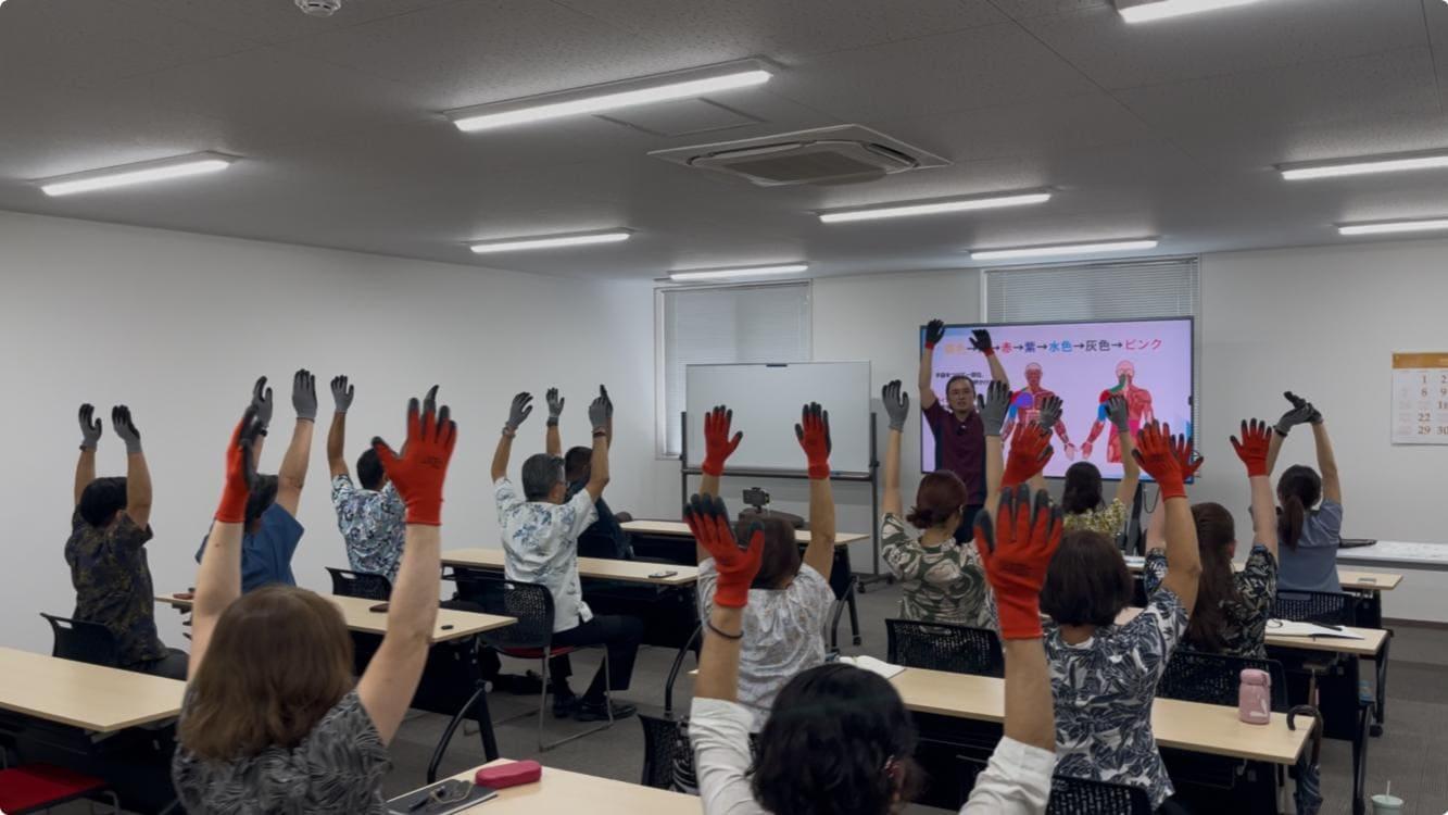 セミナーで行われた肩こり体操で講師の下里と参加者が両手を上げている風景
