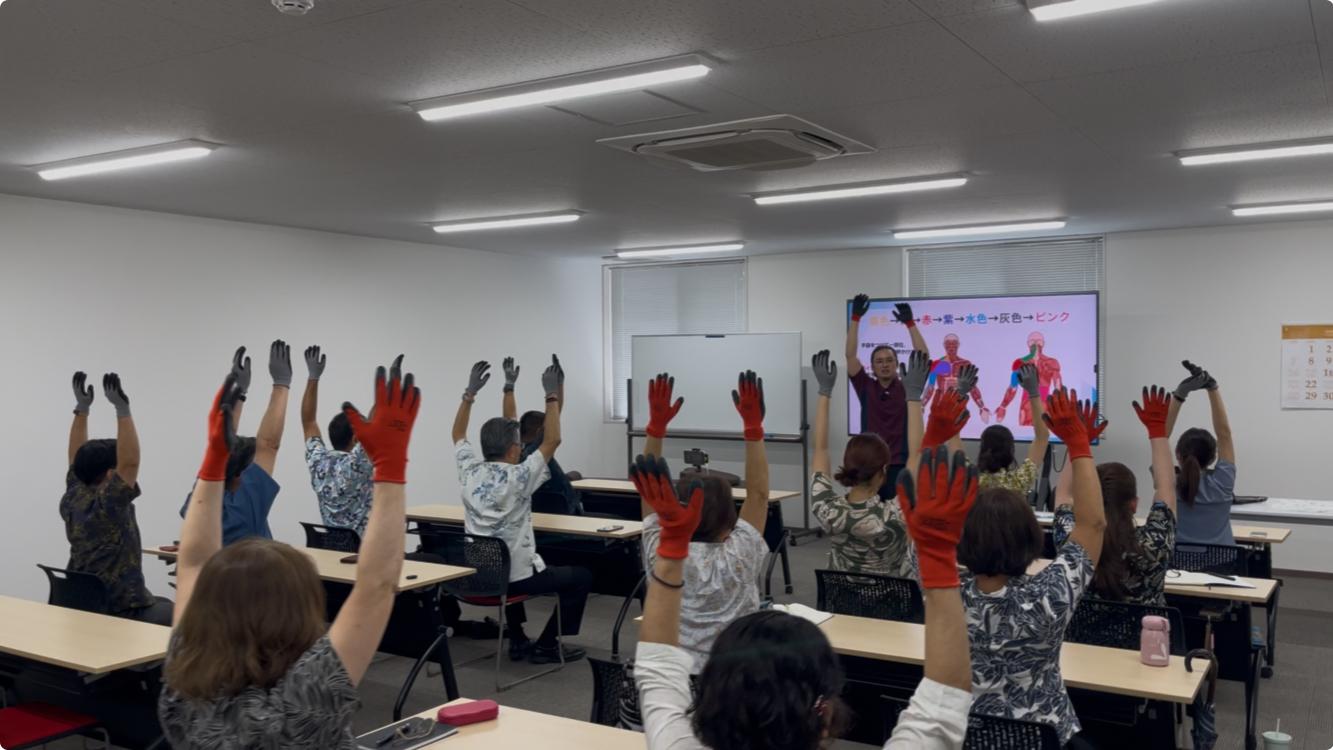 セミナーで行われた肩こり体操で講師の下里と参加者が両手を上げている風景