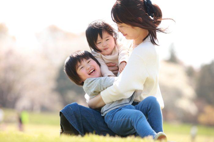 屋外で母親が二人の子供を笑顔で抱きしめる写真