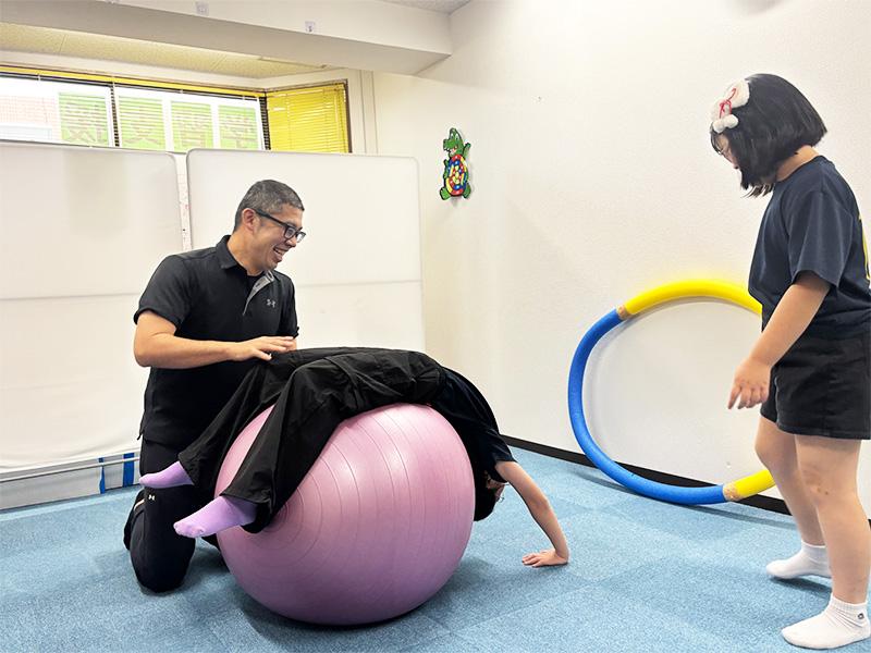 やわらキッズ運動教室で、トレーナーと一緒にバランスボールで運動する子ども