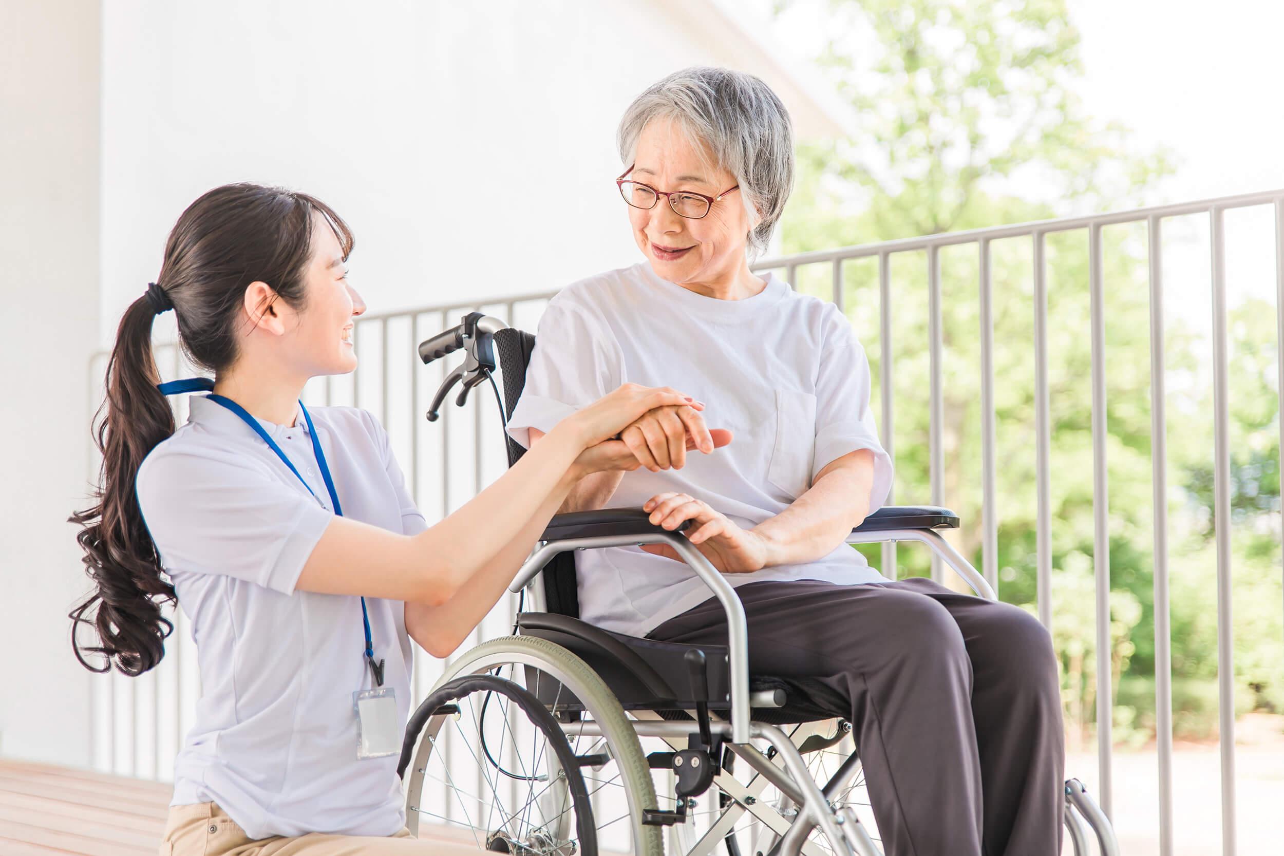 車いすにのった老人と介護者・介護職員の笑顔画像