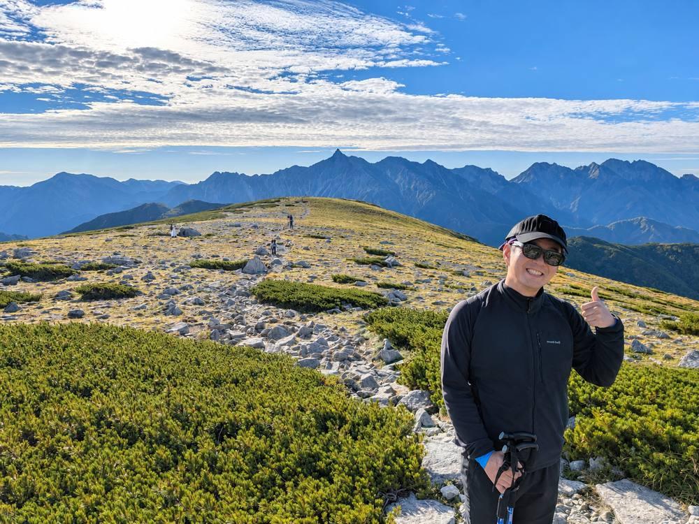 天空の滑走路で、広がる山並みを背景に笑顔を見せる佐竹宏範