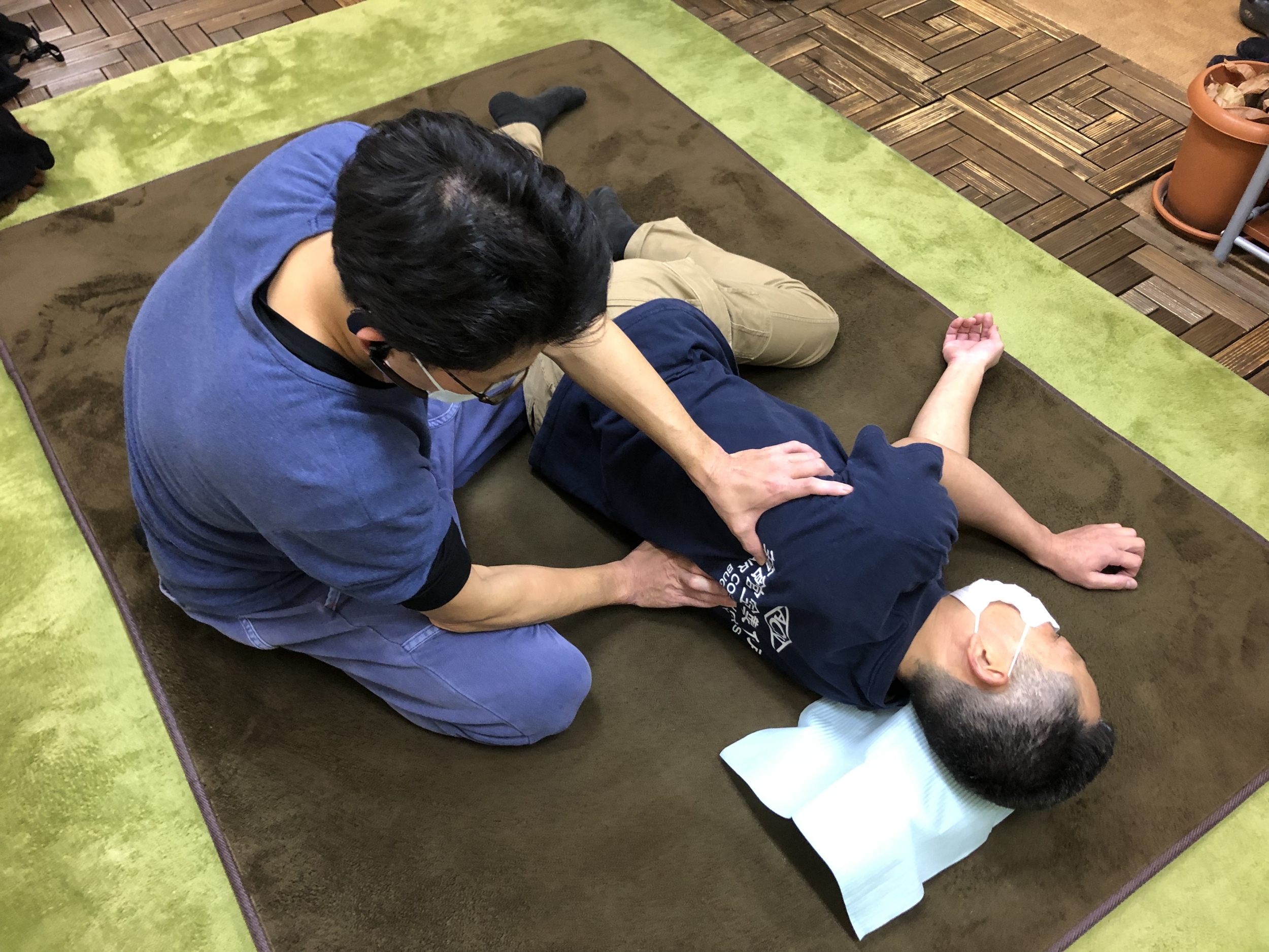 横向きに寝ている男性の背中に触っているマスクをつけた男性