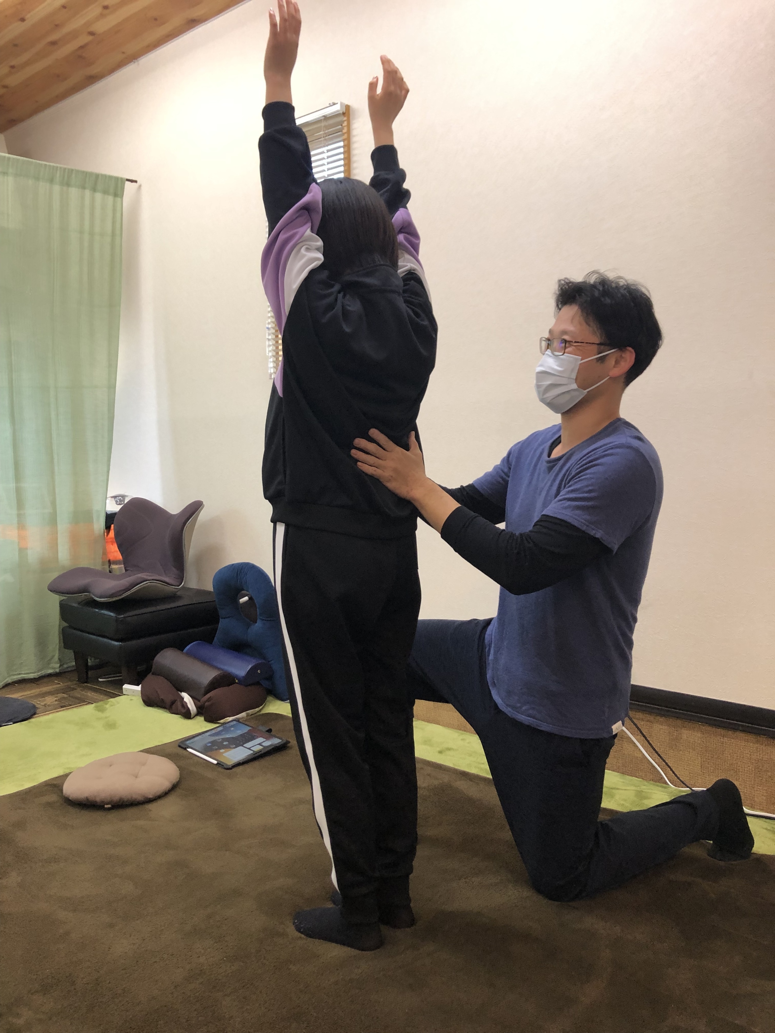 立って両手を挙げている中学生の女子の身体を片膝立ちの姿勢で支える男性