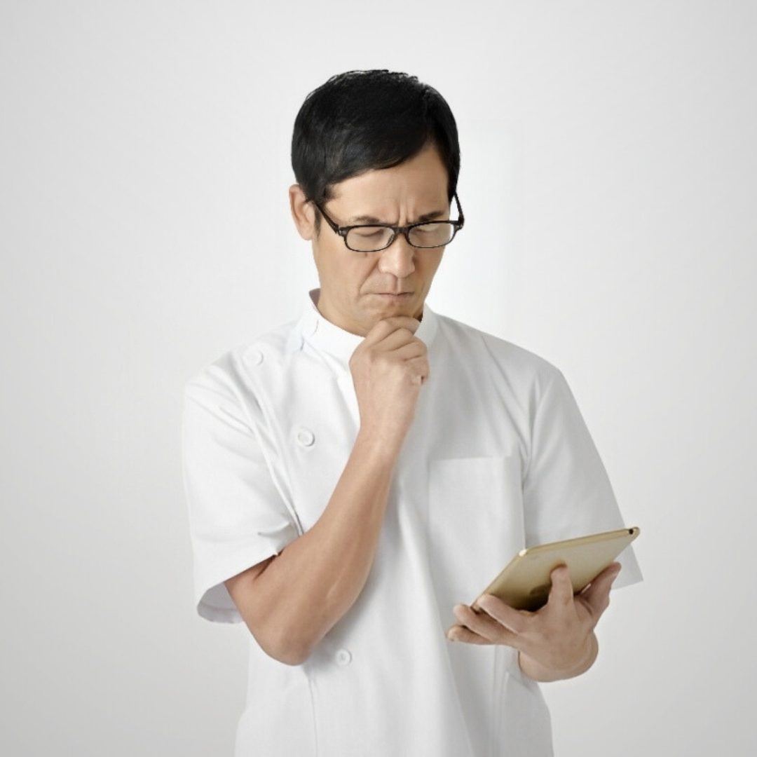 タブレットを見ながら悩む整体師。経営や集客の不安を抱えて思案している様子を表す。