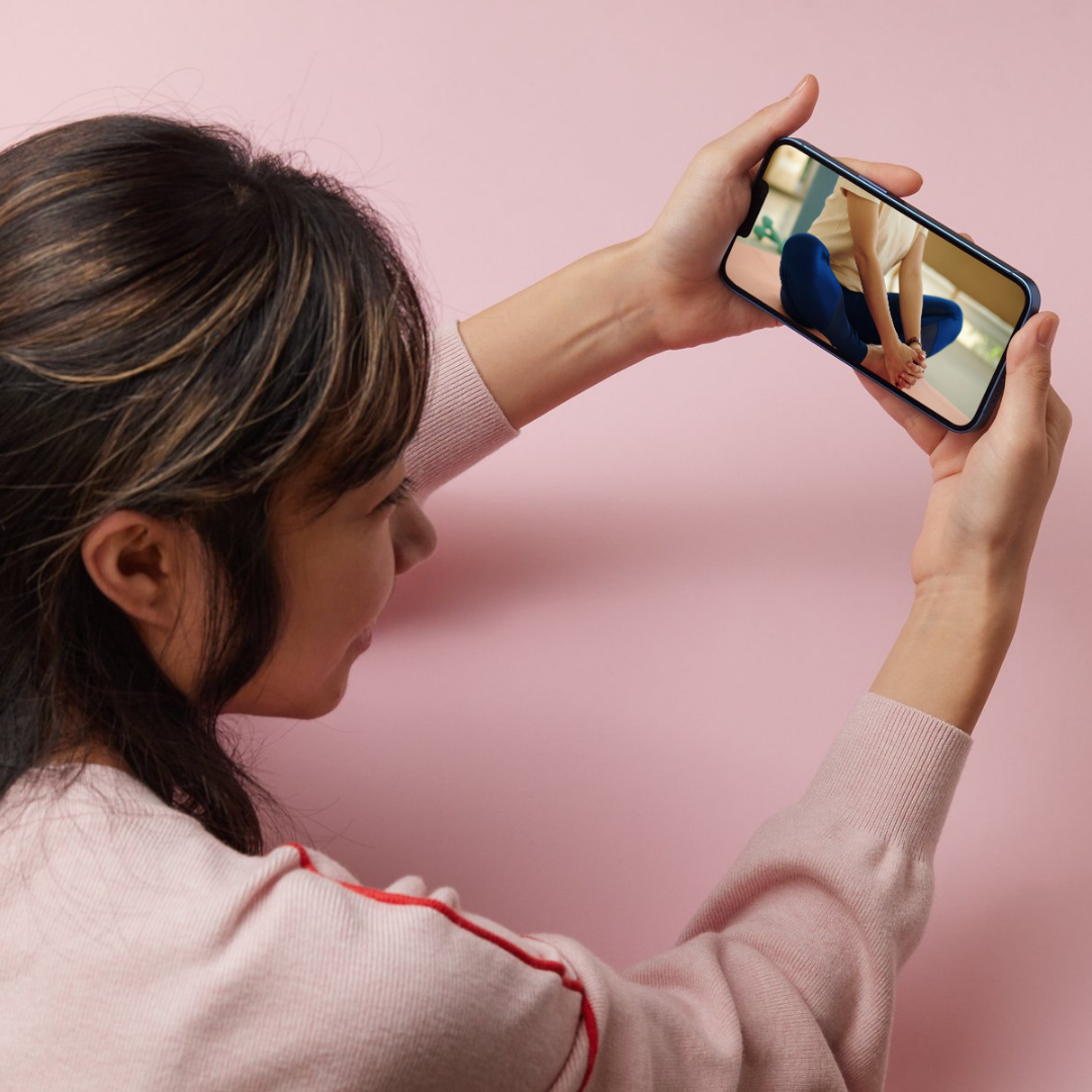 スマートフォンでセルフケア動画を視聴する女性。オンライン教材で学ぶ姿がTIM導入後の新しい仕組みを象徴している。