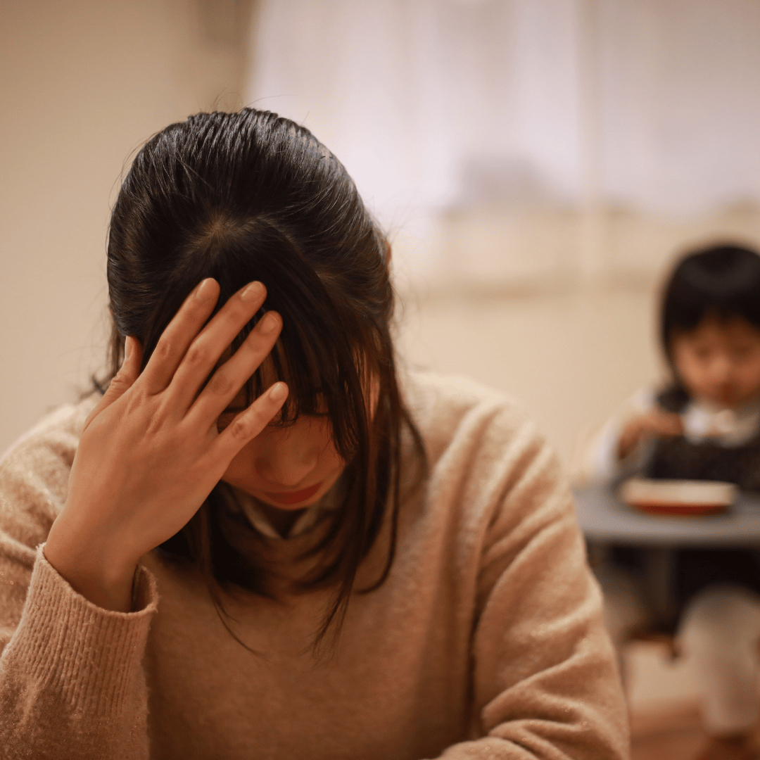 子どもの対応に疲れ、不安そうにうつむく母親の様子