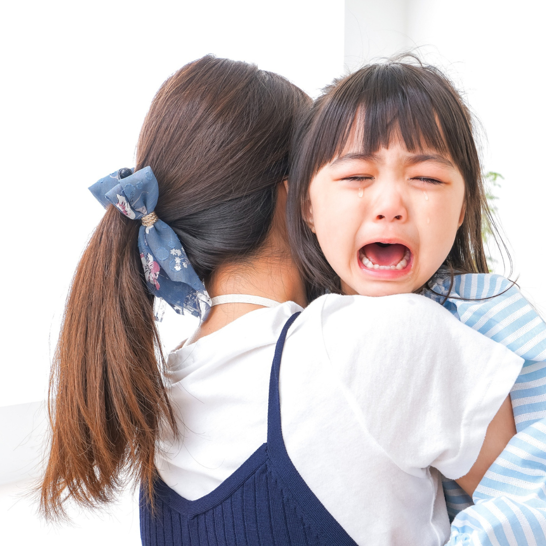 母親に抱きついて泣いている幼い女の子の写真。感情が大きく揺れた子どもを、母親が安心させようとしている場面。