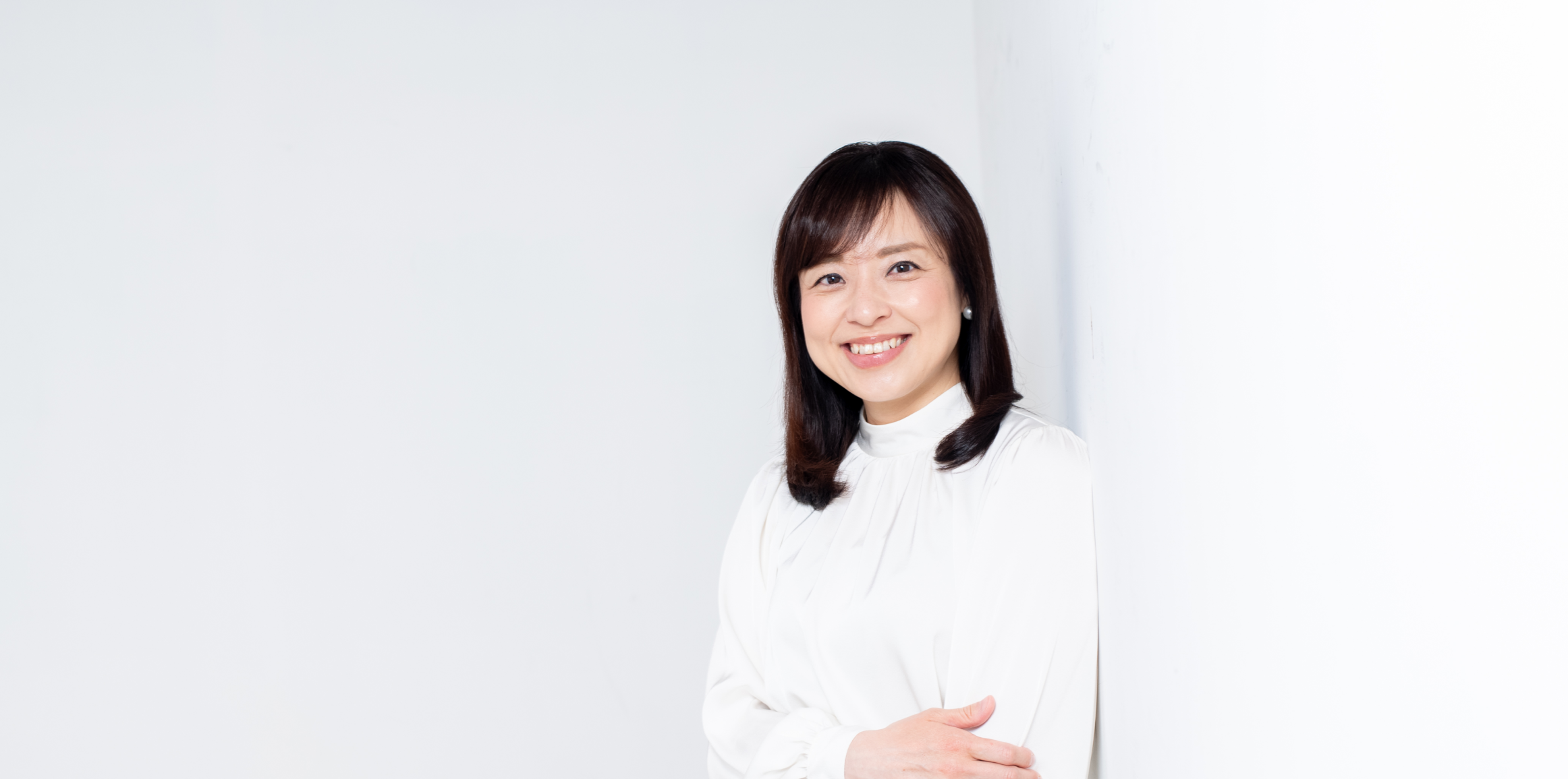 シンプルな白い背景の前で、腕を組みながら明るい笑顔を見せるフリーアナウンサー柳澤亜弓の写真。
