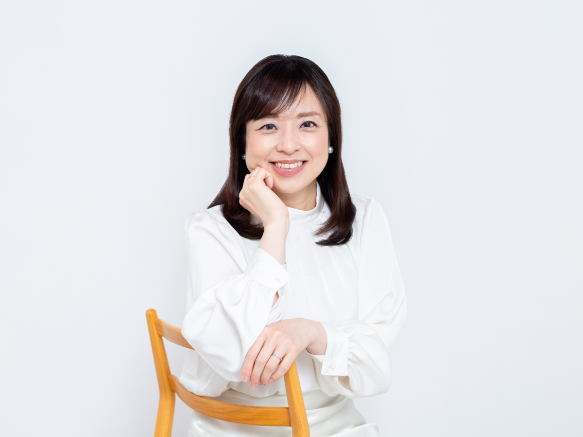 「受賞歴」セクション、白い背景の前で木製の椅子に座り、顎に手を添えて優しく微笑むフリーアナウンサー柳澤亜弓の写真。