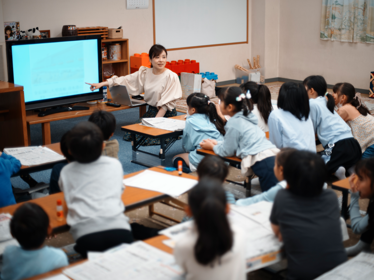 学校の教室のような場所で、たくさんの子どもたちを前にモニターを使いながら熱心に教育・地域向け講座を行う柳澤亜弓の写真。