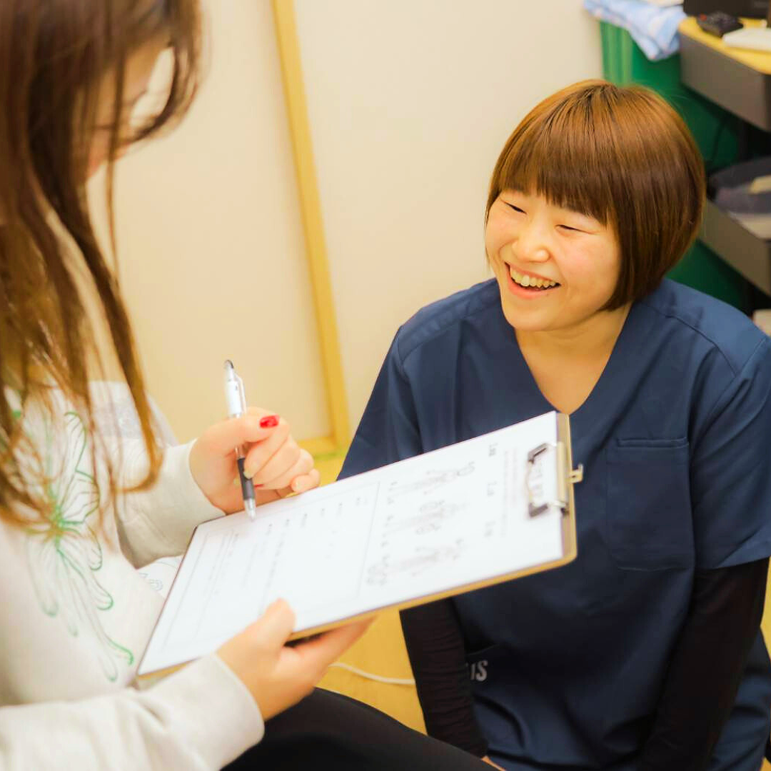 施術後に利用者と整体師がシートを見ながら笑顔で説明を交わしている様子