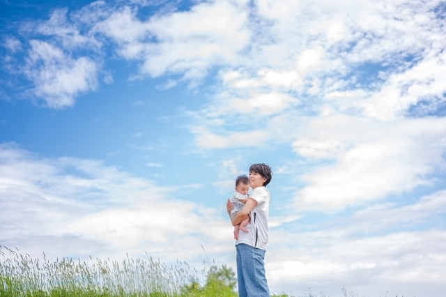 青空の下で赤ちゃんを抱く女性の画像