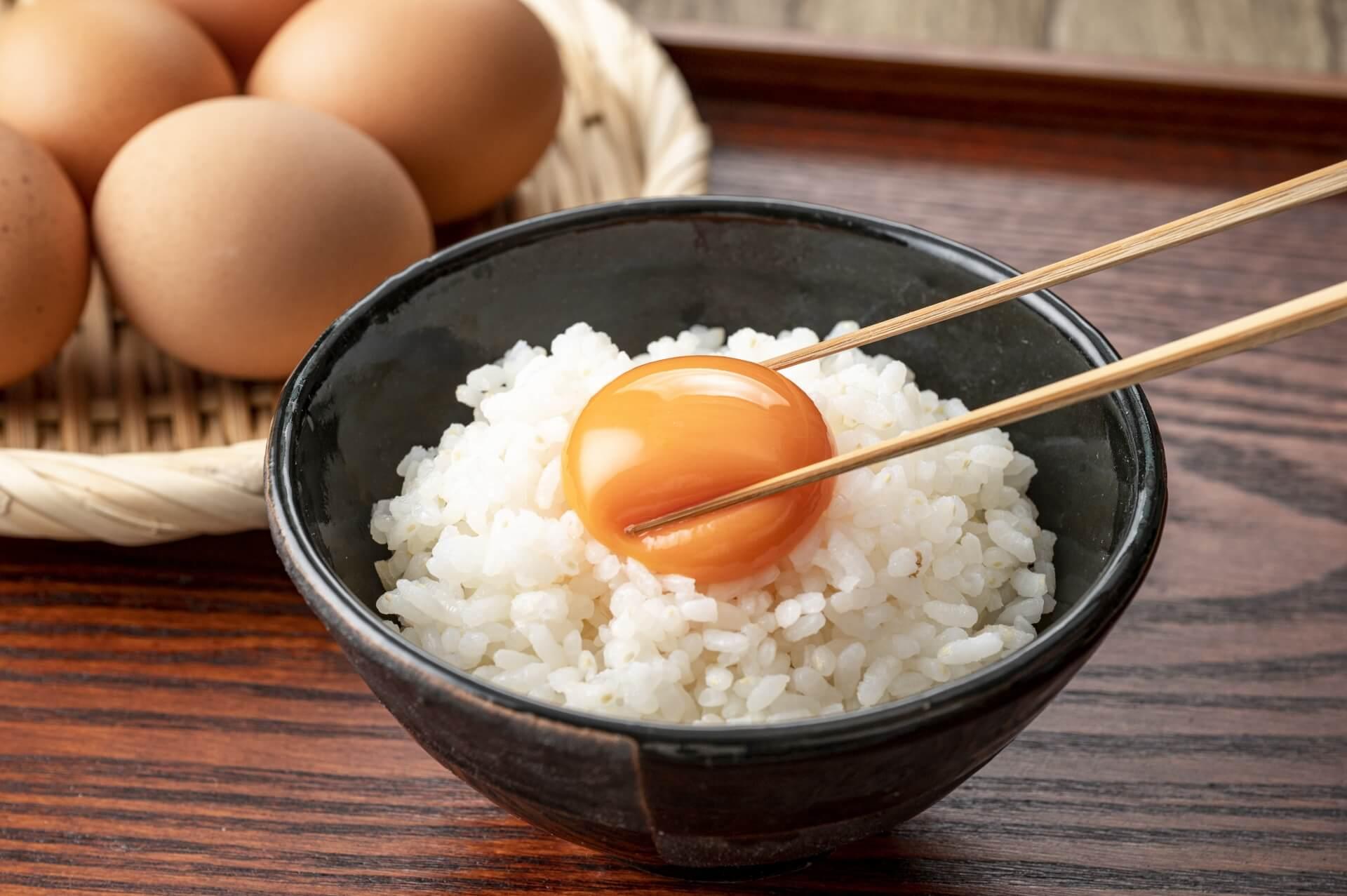 ご飯に乗った生卵を箸でつまむ