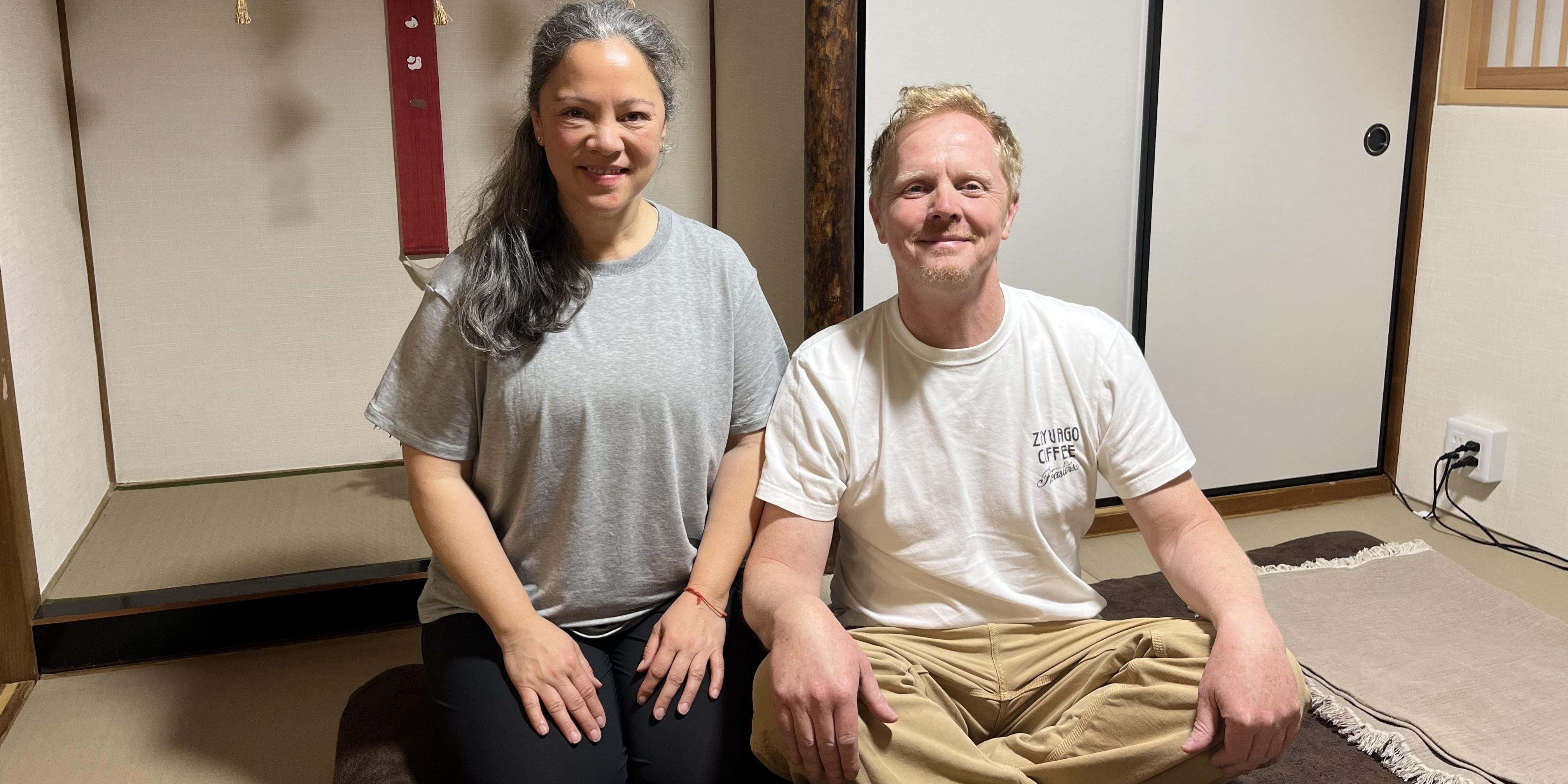 A commemorative photo of a couple from Netherlands, smiling and sitting on a futon in a traditional Japanese tatami room after their Reiki session.