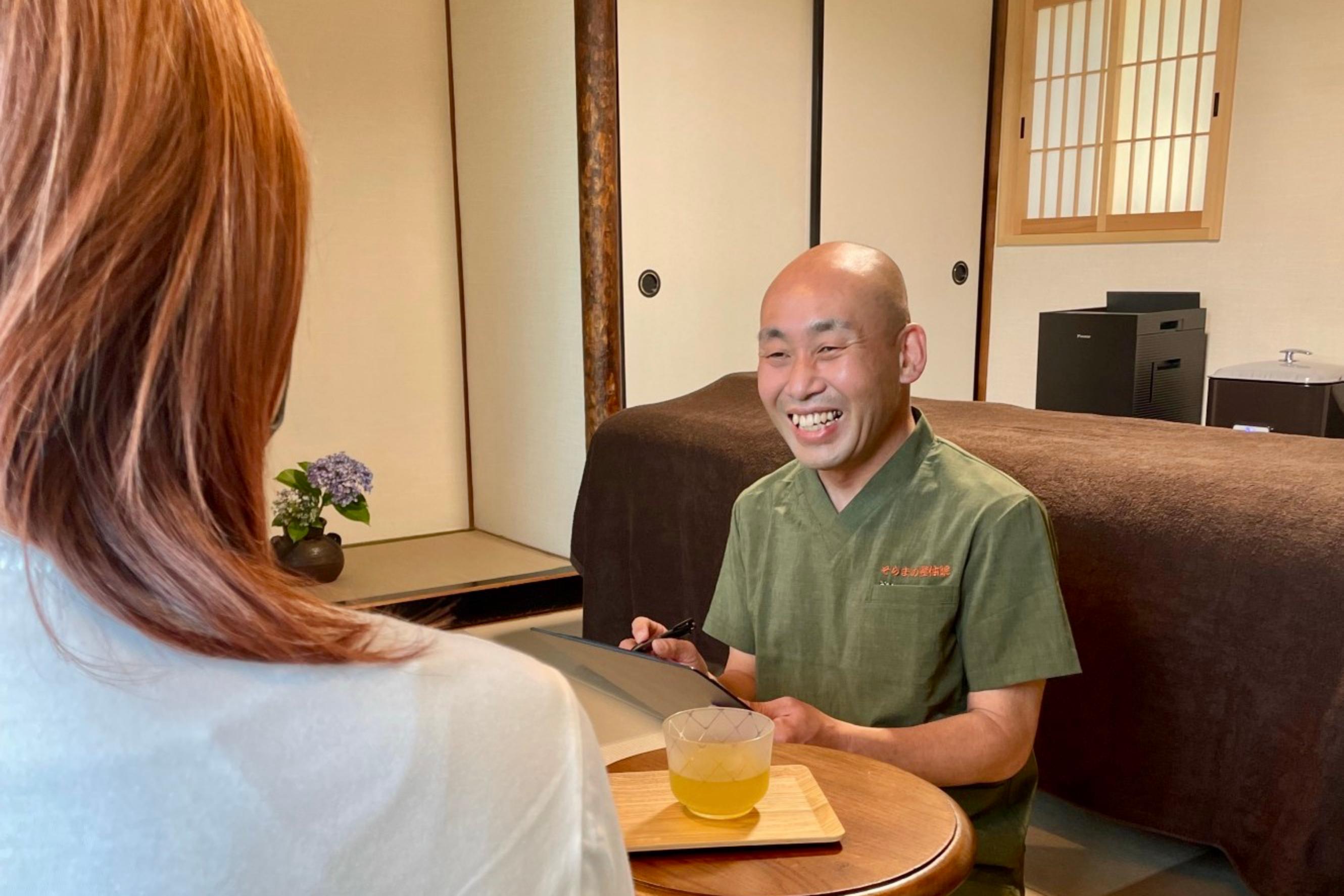 Smiling Japanese Reiki practitioner consulting with a guest in a private tatami room, offering tea before the session in Takarazuka, Japan