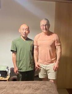 A German guest and practitioner Mizuno standing together in the clinic after a Reiki session, smiling for a commemorative photo.