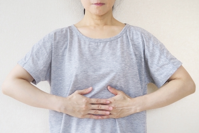 グレーのTシャツを着た人がお腹に両手を当ててセルフケアをしている様子。お腹を温めたり意識を向けるセルフケアのイメージ。