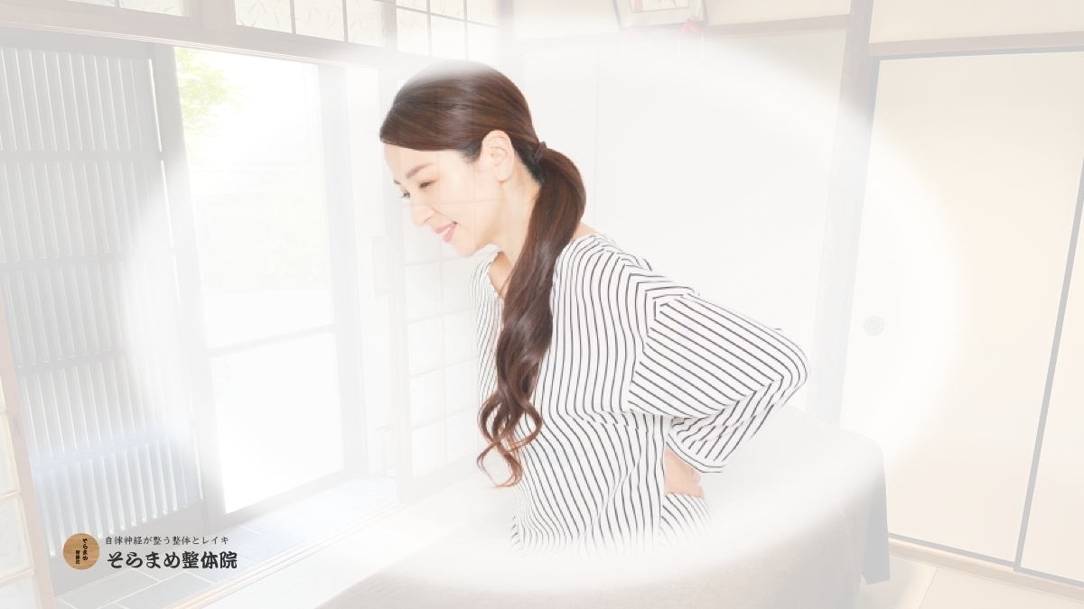 そらまめ整体院の和室の施術室を背景にした、背中を押さえる女性の写真。ストレスや自律神経の乱れによる背中のこわばり・姿勢の崩れをイメージ。穏やかな光の中で心身を整える様子。