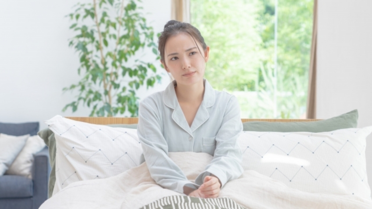 薬を飲んでも眠れない不眠に悩み、布団の上で考え込む女性。
