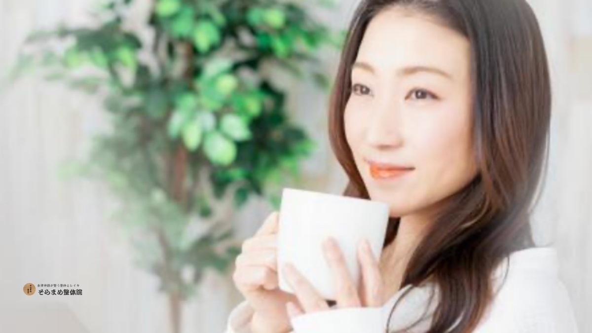柔らかな光の中で白いマグカップを持ち、リラックスした表情で微笑む40代の女性。背景には観葉植物があり、穏やかな日常のひとときを表現。｜そらまめ整体院のブログメイン画像