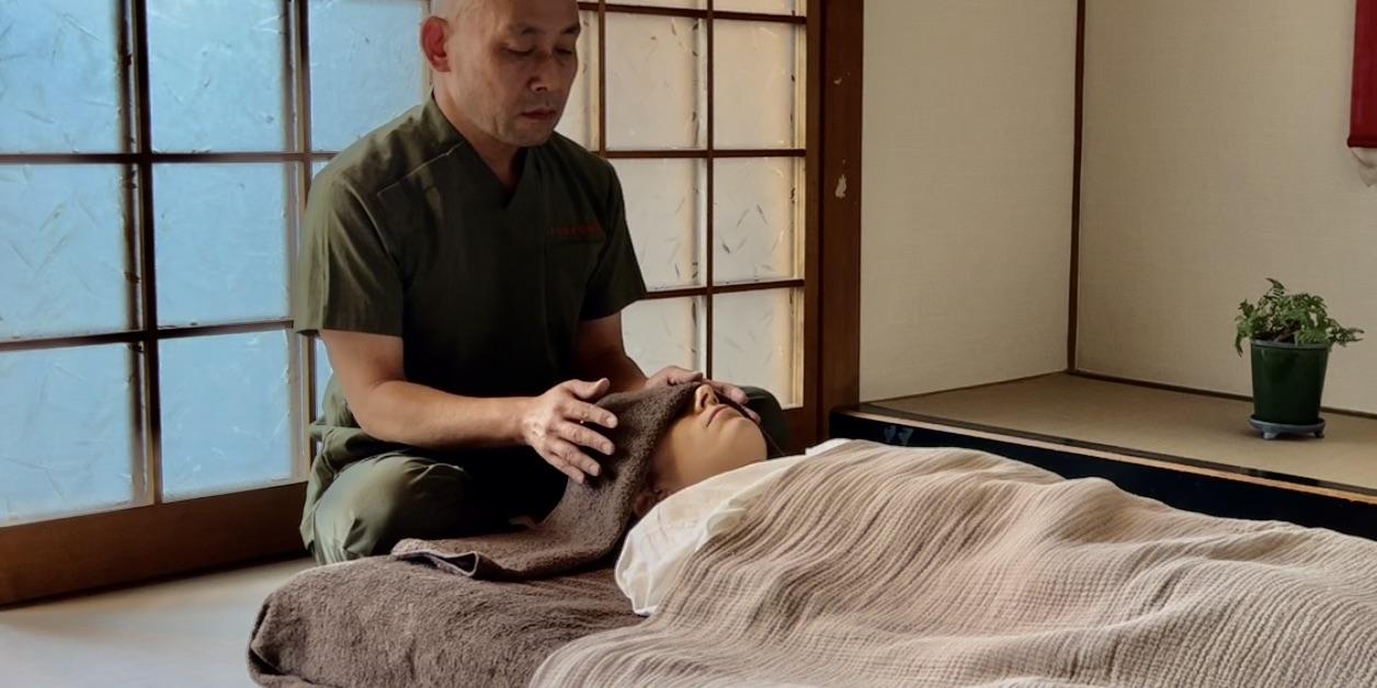 A practitioner placing hands near a client's head during a Reiki session in a traditional Japanese room.