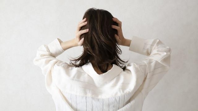耳鳴りや頭の重さに悩み、両手で頭を抱える女性の後ろ姿｜宝塚の自律神経専門・そらまめ整体院