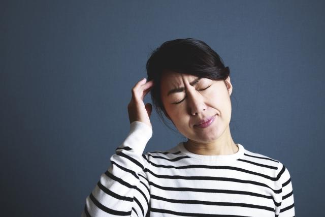 片頭痛があり、右手を頭に当てながら辛そうな表情をしている女性