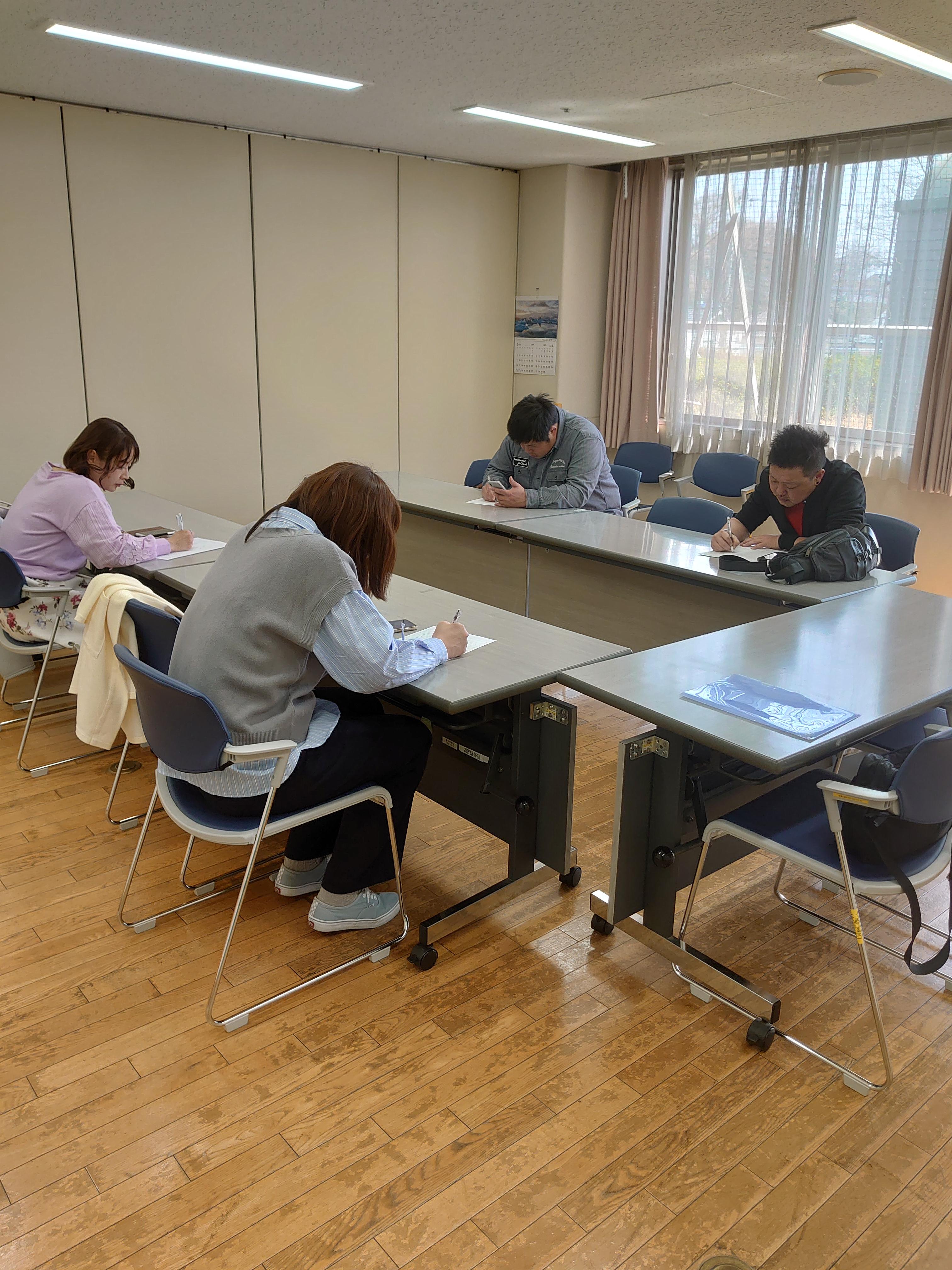 男性2名、女性2名が椅子に座り、机で書類を書いている