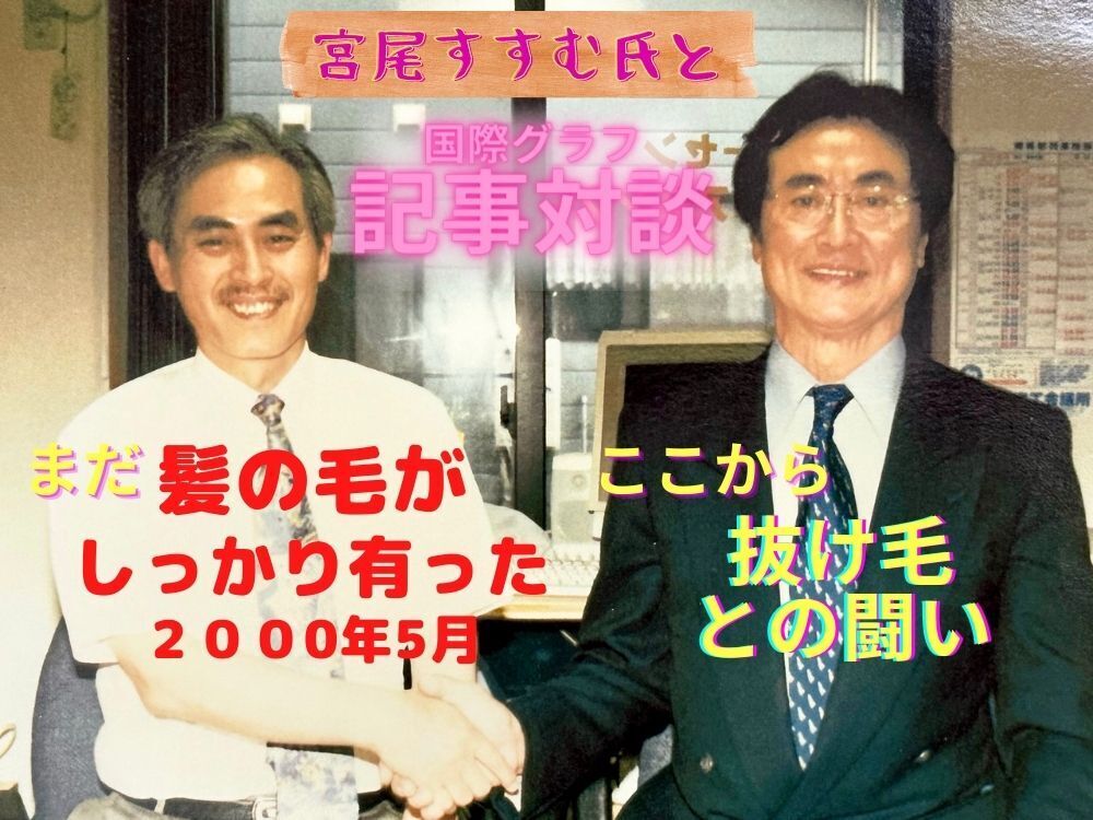 2000年5月に国際グラフの記事取材でご来社いただいた（故）宮尾すすむさんと佐藤社長が握手している写真です。
