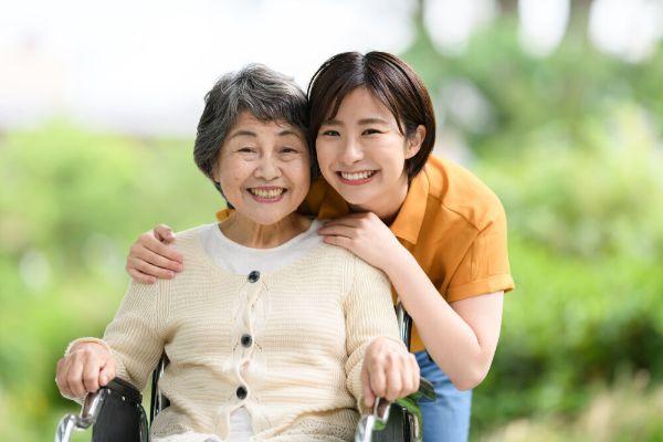シニア女性とその肩に手を当てて親しそうにしている若い女性が二人でほほ笑む写真