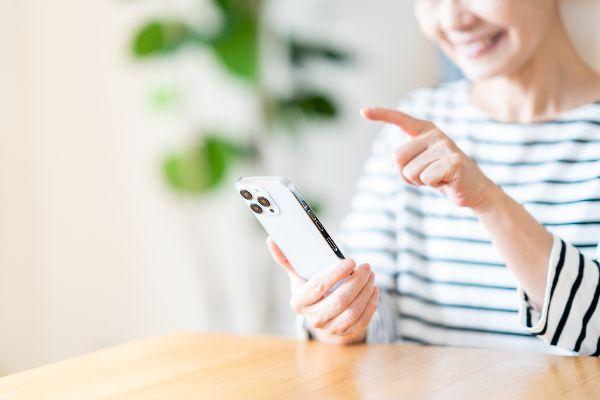 明るい部屋を背景に笑顔でスマホを操作する健康的なシニア女性